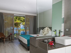 A modern hotel room with a balcony, a bed, a sitting area, and a large bathroom.
