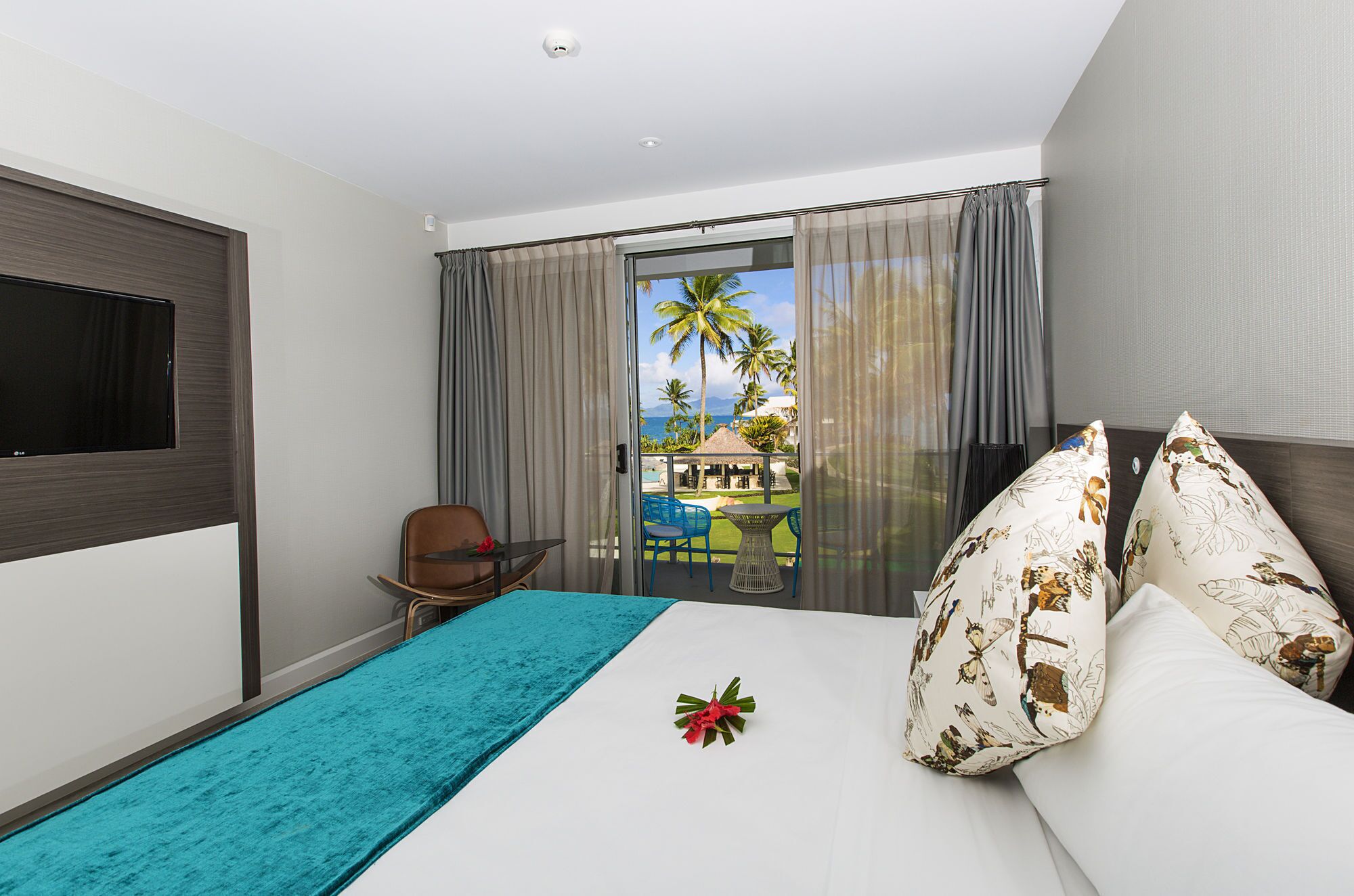 Habitación de hotel con cama, televisión, balcón con mesa y sillas, y vista al océano.