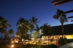 A resort with a pool, palm trees, and a building with illuminated windows.