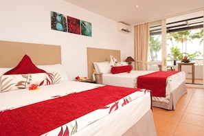A hotel room with two beds, a minibar, a desk, and a view of palm trees.
