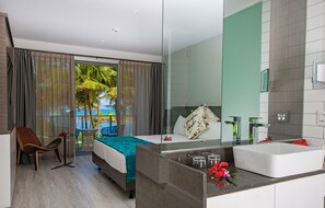 A hotel room with a bed, a bathroom with a large mirror, and a view of palm trees through the window.