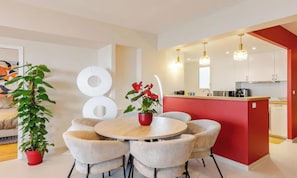 Uma cozinha moderna com uma parede de destaque vermelha, uma área de refeições com mesa e cadeiras redondas e um vaso de planta.