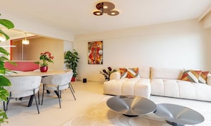Uma sala de estar moderna com um sofá, uma mesa de jantar com cadeiras, uma mesa de centro e um quadro na parede.