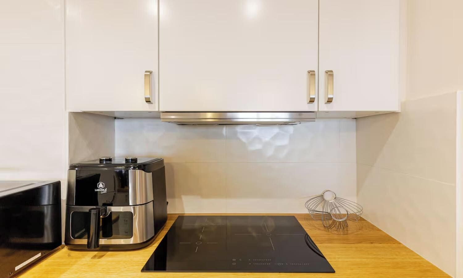 Eine kleine Küche mit weißen Schränken, einer schwarzen Kochfeld mit Induktion und einer Kaffeemaschine.