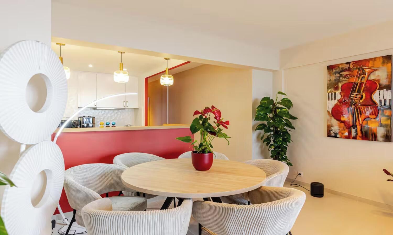 A modern dining area with a round table, white chairs, and a red vase with flowers.