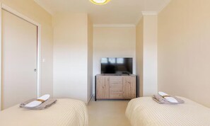 Quarto de hotel com duas camas, uma televisão sobre um armário de madeira e uma porta.