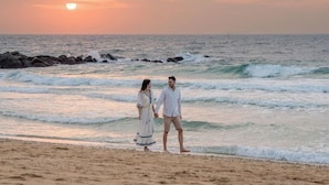 A couple walking on a beach with waves and a sunset in the background. - Banyan Tree Dubai (Dubai)