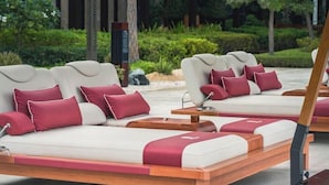 A row of modern lounge chairs with white cushions and red accents, arranged outdoors with a view of a landscaped garden. - Banyan Tree Dubai (Dubai)