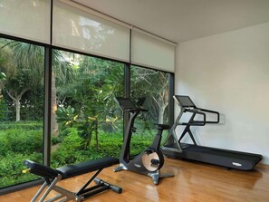 A gym with exercise equipment, large windows, and a view of greenery. - Banyan Tree Dubai (Dubai)