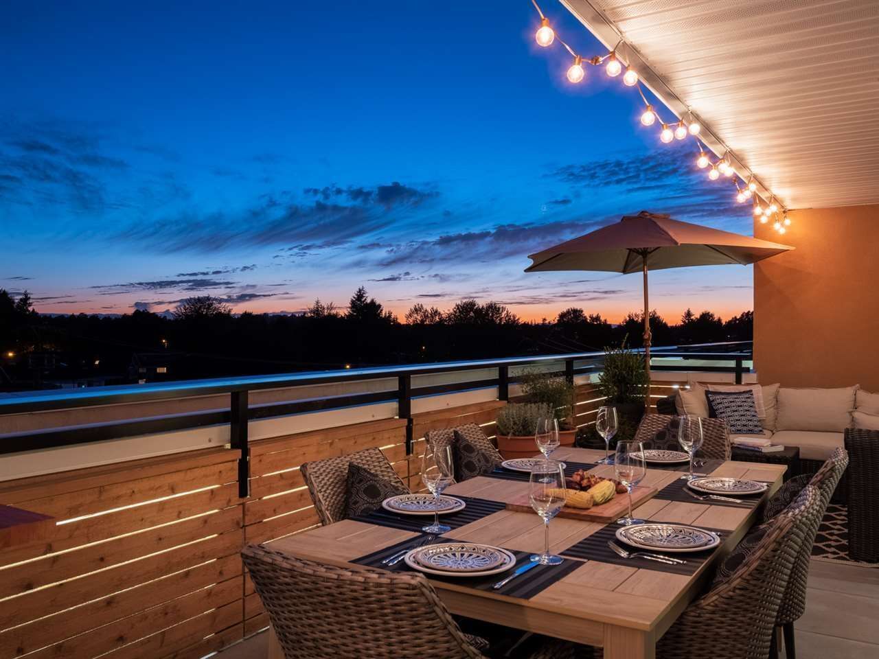An outdoor dining area with tables and chairs, a view of the sky, and string lights.