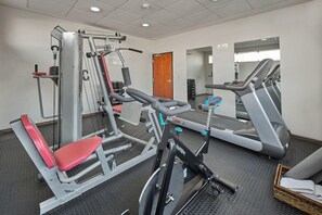 Una palestra con diverse attrezzature per esercizi, tra cui una panca per pesi, una pressa per le gambe e un tapis roulant.