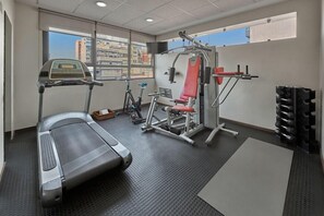 Una palestra con tapis roulant, macchinari per pesi e una finestra vista città.