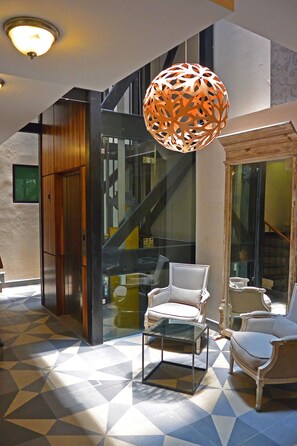 Un vestíbulo con suelo de diseño geométrico, una escalera y dos sillones tapizados.