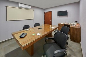 Un salón de conferencias con una larga mesa, sillas, una pantalla de proyector, un televisor y una puerta.