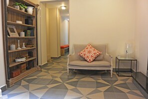 Una habitación con piso estampado, una silla con un cojín decorativo, una estantería y una pequeña mesa con dispensador de agua.