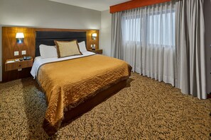 Una camera d'hotel con un letto grande, due comodini con lampade, una finestra con tende e una moquette decorata.