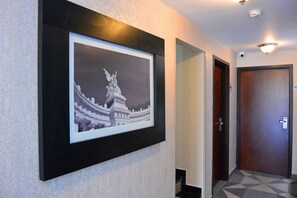 Un pasillo con una fotografía en blanco y negro enmarcada en la pared, una puerta y un papel tapiz estampado.
