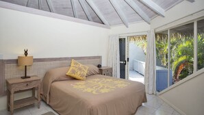 A bedroom with a bed, bedside table, lamp, and a view of palm trees through a glass door. - Te Manava Luxury Villas Spa (Rarotonga)