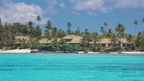 A beachfront property with thatched-roof buildings, palm trees, and a clear blue sea. - Te Manava Luxury Villas Spa (Rarotonga)