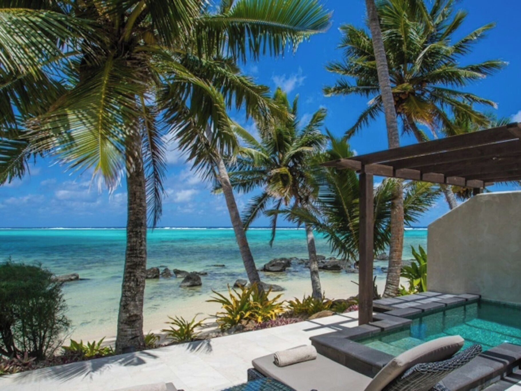 A pool area with lounge chairs, palm trees, and a view of the ocean.