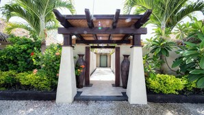 A covered walkway with a thatched roof, flanked by large vases and surrounded by lush greenery. - Te Manava Luxury Villas Spa (Rarotonga)
