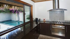 A modern kitchen with a built-in stove, oven, and a large window overlooking a pool area. - Te Manava Luxury Villas Spa (Rarotonga)