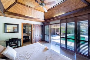 Un dormitorio amplio con una cama grande, techo de madera y vista a una piscina a través de puertas corredizas de vidrio.
