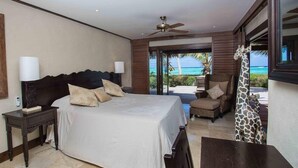 A bedroom with a bed, nightstands, a ceiling fan, and a view of the ocean. - Te Manava Luxury Villas Spa (Rarotonga)