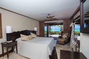 Un dormitorio con cama, mesitas de noche, ventilador de techo y vista al océano.