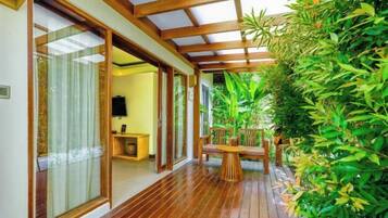 A wooden deck with a glass door leading to a room, surrounded by lush greenery.