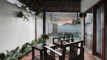 A covered outdoor seating area with a table and chairs, overlooking a pool and a mountainous landscape.