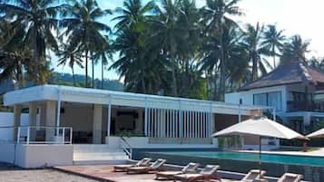 Un área de piscina con sillas de descanso y sombrillas, rodeada de palmeras.