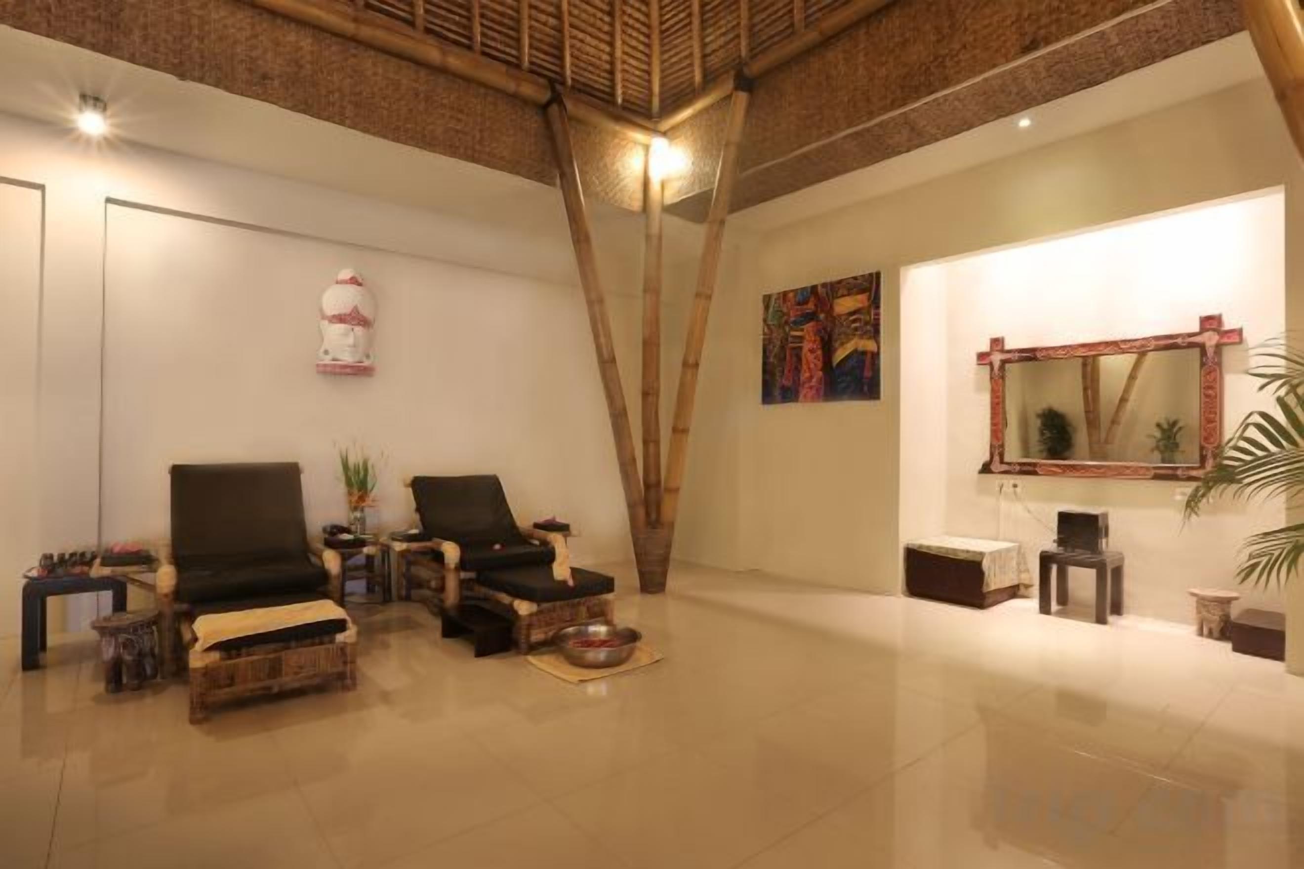 Une pièce spacieuse avec un plafond haut, un grand miroir et un coin salon comprenant deux fauteuils et une petite table.