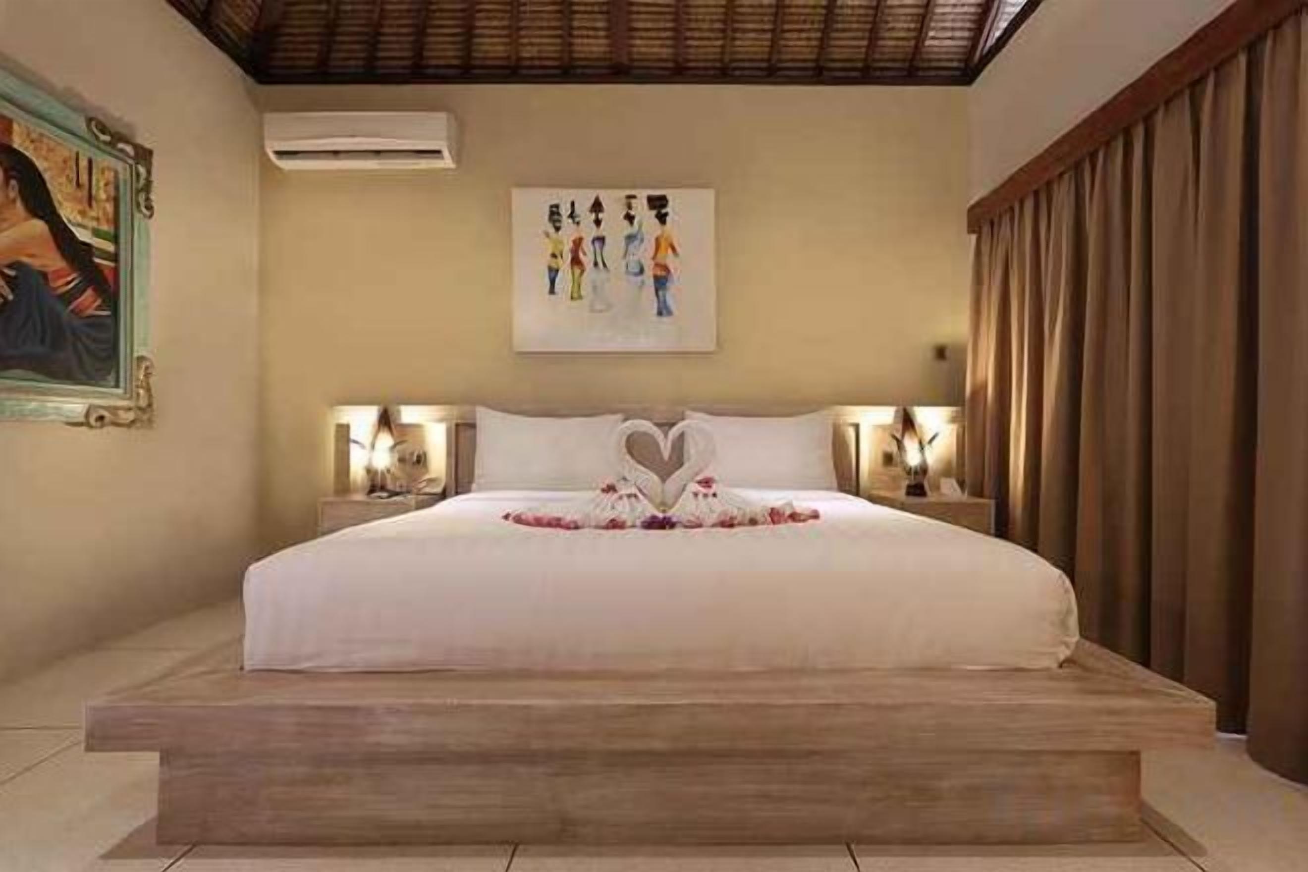 A hotel room with a large bed, a painting on the wall, and a decorative heart on the bed.