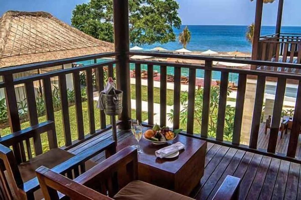 Una terraza de madera con una mesa y sillas, con vistas a una playa y el océano.