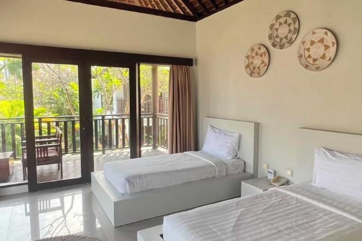 A hotel room with two beds, a balcony, and a view of greenery.