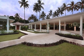 Un edificio moderno con un paseo cubierto, palmeras y un césped cuidado.