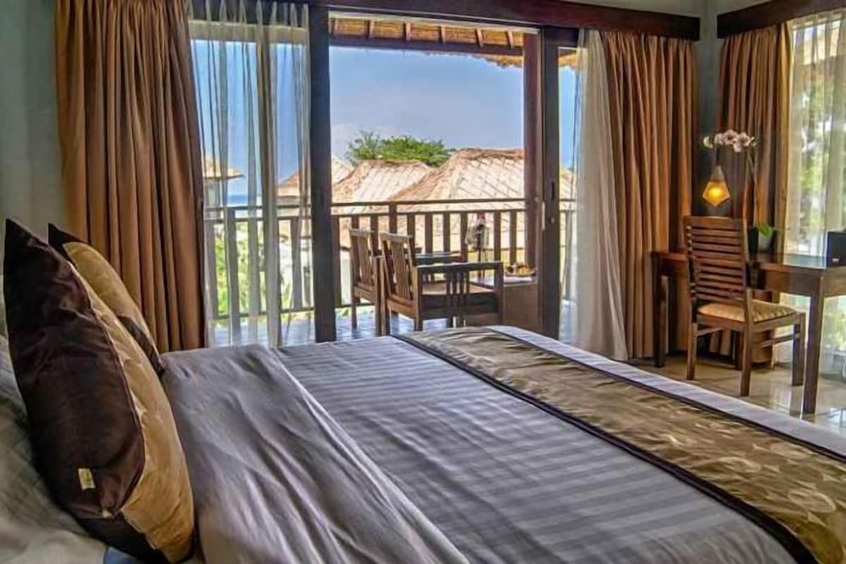 A bedroom with a bed, a table, and chairs, and a balcony with a view.