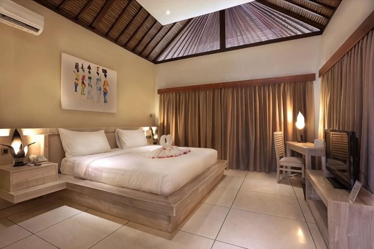 A hotel room with a large bed, a desk, a chair, and a television.