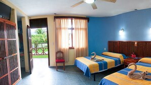 Une chambre avec deux lits, un ventilateur de plafond, une fenêtre avec des rideaux et une vue sur la verdure.