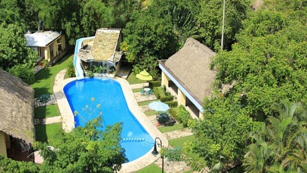 Une piscine entourée d’une végétation luxuriante et un bâtiment à toit de chaume.
