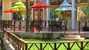 Un espace extérieur aménagé pour les repas, avec des tables, des chaises, des parasols et une rambarde.