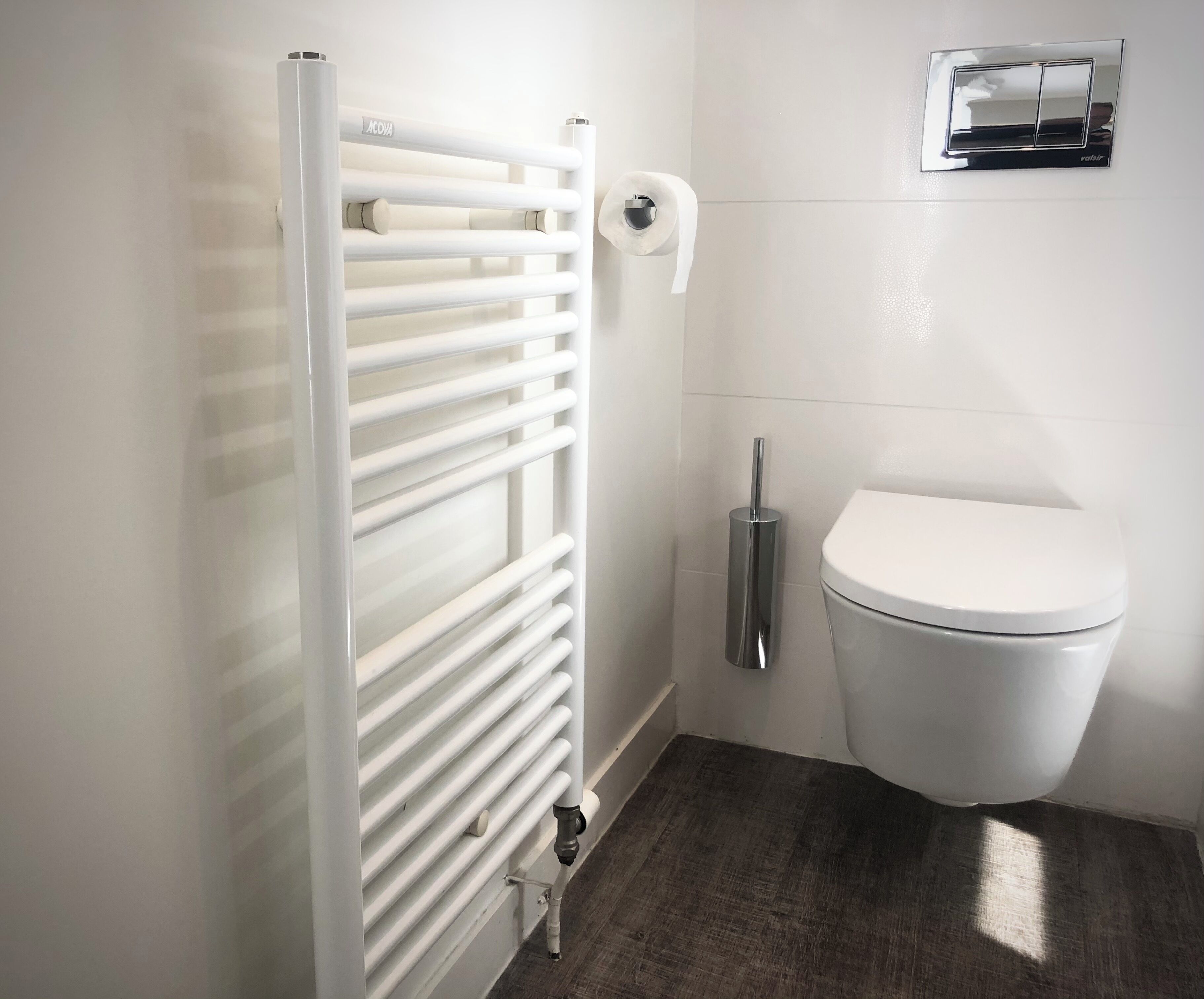 A bathroom with a white radiator, a toilet, and a hand dryer.