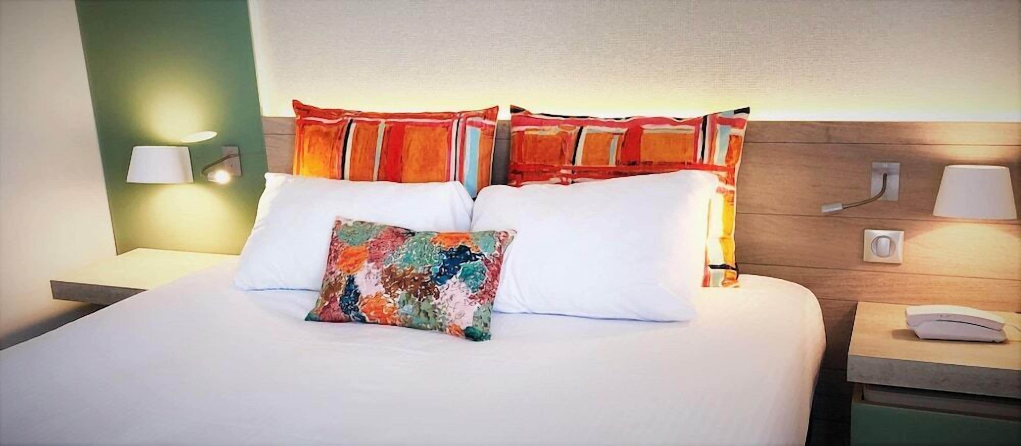 A hotel room with a bed, two bedside lamps, a nightstand, and a wall-mounted lamp.