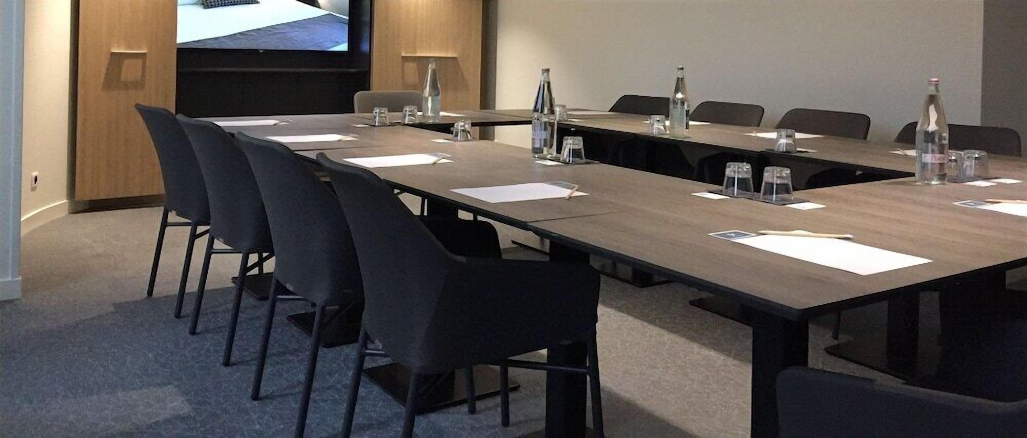 A conference room with a long table, chairs, and a large screen.