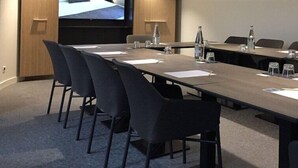 Una sala de conferencias con una larga mesa, sillas y una pantalla grande.