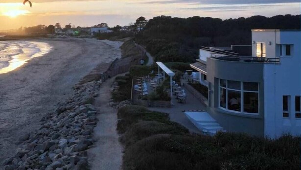 Un hotel frente al mar con vistas a la playa, mobiliario exterior y una estructura moderna.