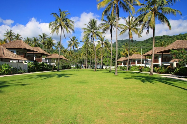 A resort with thatched-roof bungalows, a well-maintained lawn, and palm trees. - Living Asia Resort Spa Lombok (Senggigi)