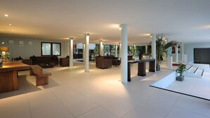 Een ruime woonkamer met een hoge plafond, diverse zithoeken en een groot raam dat voor natuurlijk licht zorgt.