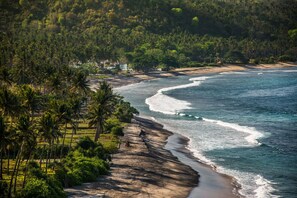A coastal landscape with a beach, palm trees, and a view of the ocean. - Living Asia Resort Spa Lombok (Senggigi)